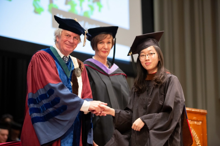 A man shakes hands with a young woman in traditional graduation robes