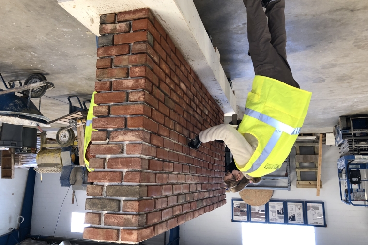 person works on mortar on a small brick wall in a studio