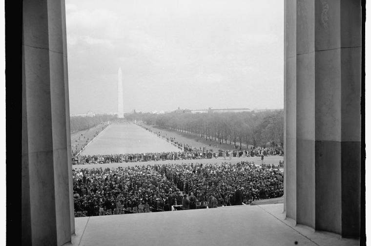 Archival black and white photo looking between columns at crowd in