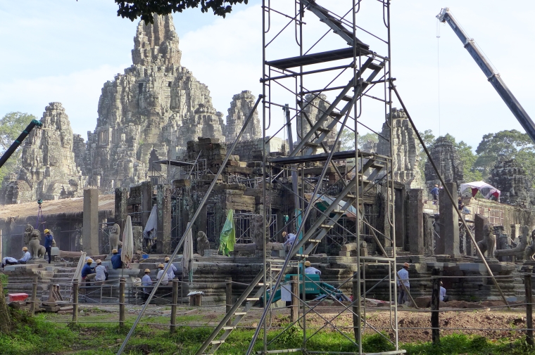 Workers in hard hats operate machinery at a stone temple