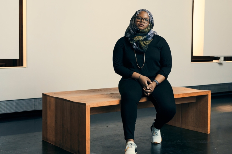 Photo portrait of artist Kameelah Janan Rasheed sitting on a bench in a museum-like setting