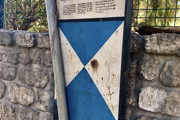 Metal Blue Shield sign on brick wall with bullet holes