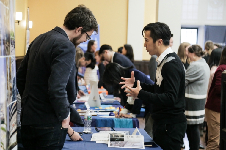 Two standing men conversing across a table with brochures.