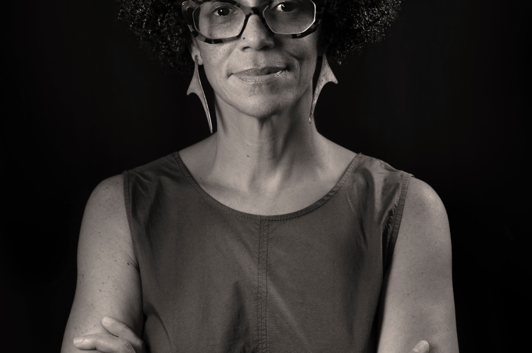 black and white headshot with arms folded across the chest, staring forward