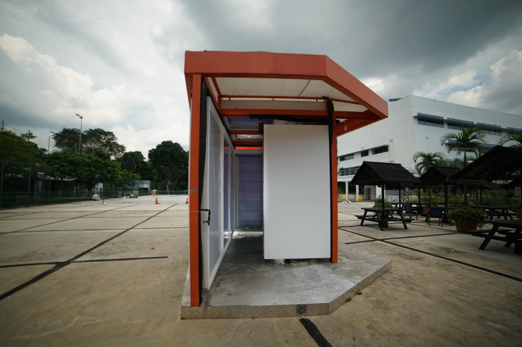 A white and orange painted room-size pavilion made of radiant cooling panels is positioned in a site in Singapore. 
