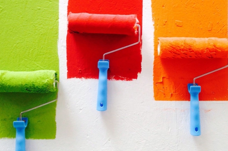 Green, red, adn oragnge paint rollers on a white background.