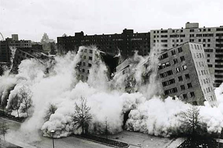 Black and white photo of several tall buildings collapsing in a demolition.
