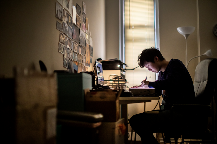 Dennis Kim draws at his desk with printed images on the wall he faces