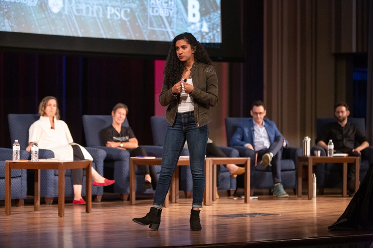 Varshini Prakash on stage at Irvine Auditorium with four speakers seated behind.