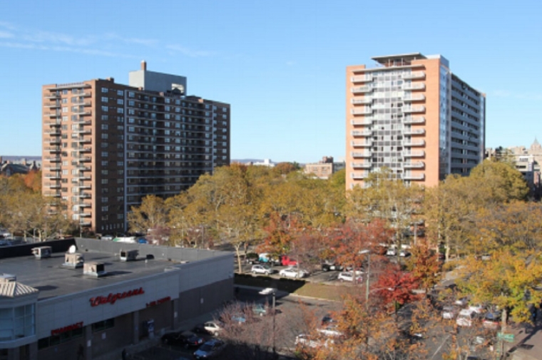 Two apartment building towers next to a Wallgreens with trees in fall folliage below