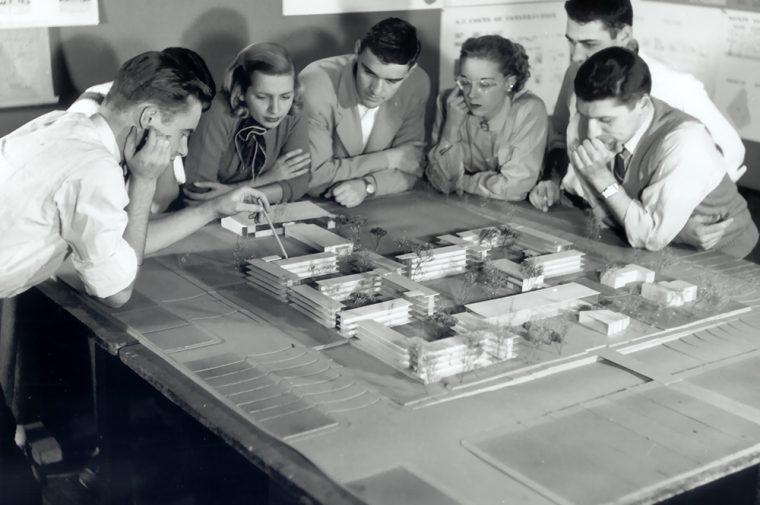 A group of students and faculty gather around an architectural model