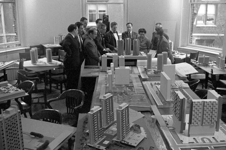 A group of people are gathered around architectural models sitting on tables