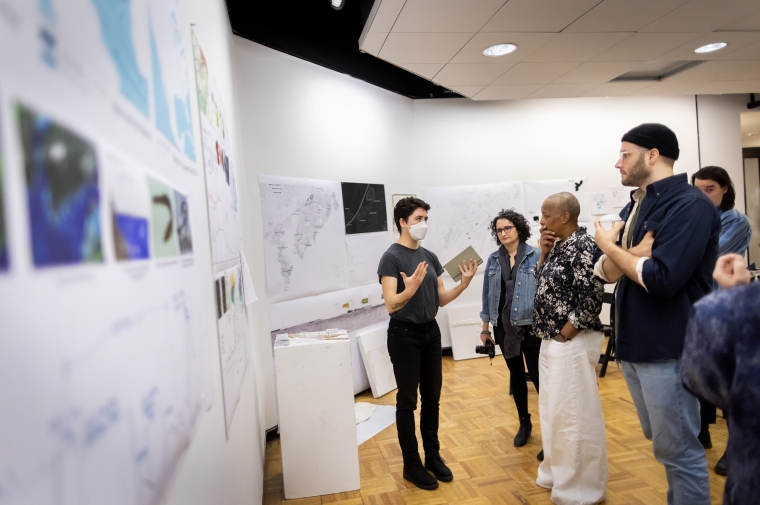 Young person in front of group gestures at posters on wall behind