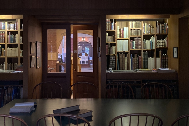 Book lined, illuminated shelves face a wood table and chairs