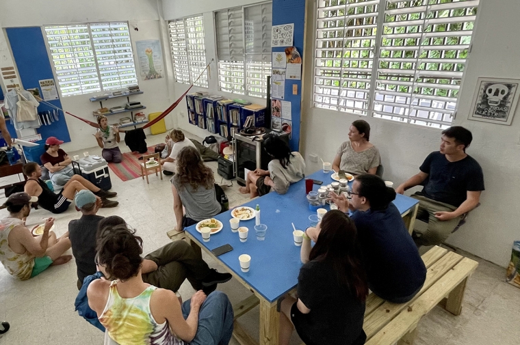 A group of students sit and listen to a presentation while eating a meal