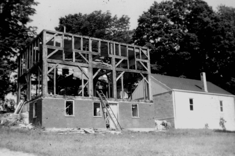 black and white photo of a house being built, 2 story wooden frame 