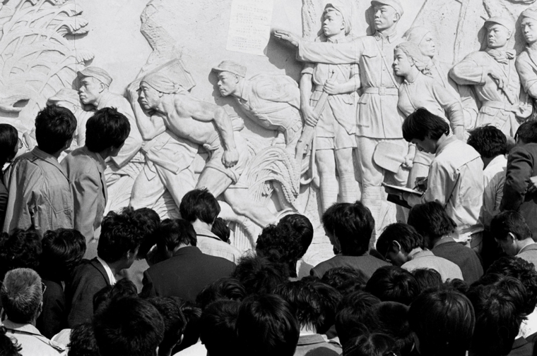black and white photo, backs of heads facing a statue in relief