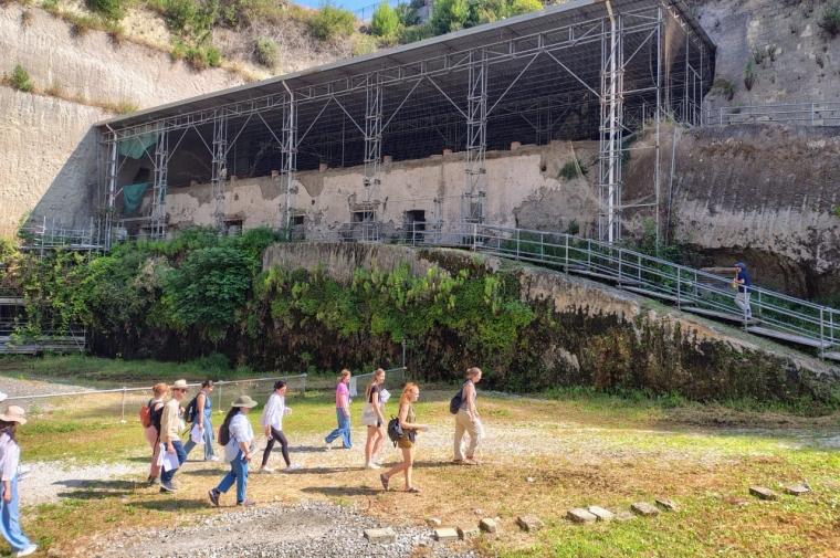 Several figures walk in front of archaeological ruins of ancient city