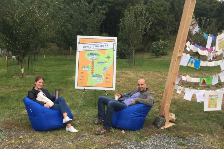 Visitors to Bartram's Garden Harvest Fest relax and enjoy seating at the Neighborhood Exchange Box installation, which includes signage about Reimagining the Civic Commons