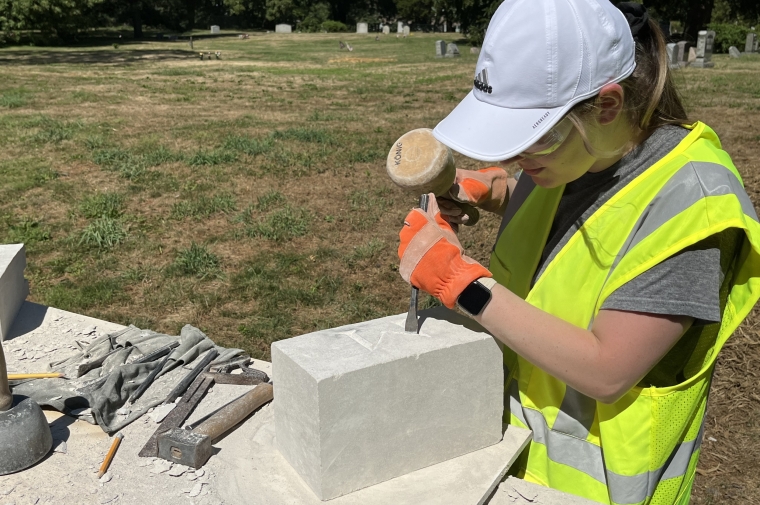 person uses chisel to carve letter into stone block