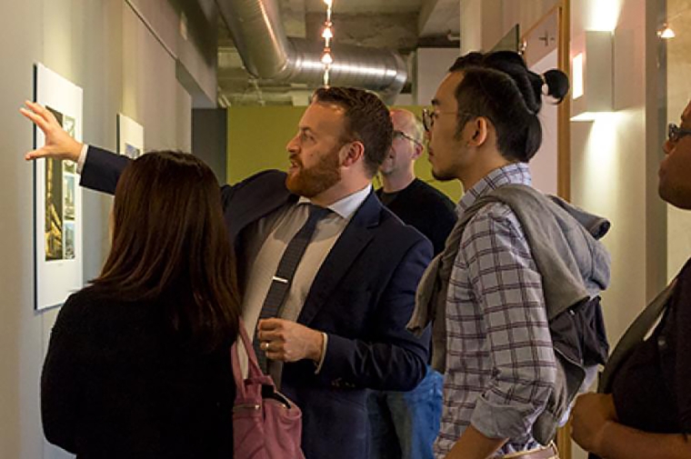 A person points at work on a wall to a group of people