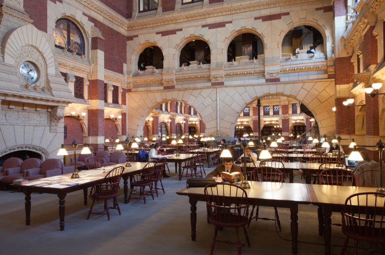 Huge library space with stone arched architecture and several students working at large wooden tables