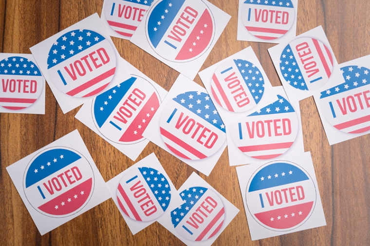 Round red, white, and blue "I VOTED" stickers on a wooden table