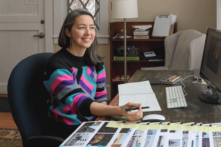 jane mah hutton is seated at a desk 