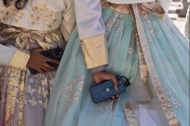 Closeup of woman in silk dress clutching iPhone behind her back