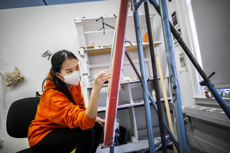 The artist working on a painting in her studio while wearing a mask