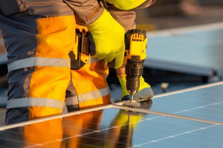 Worker in yellow uniform drilling into solar panel