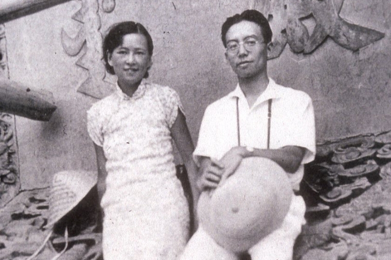 Two young Asian people standing on a tile roof pose for photo