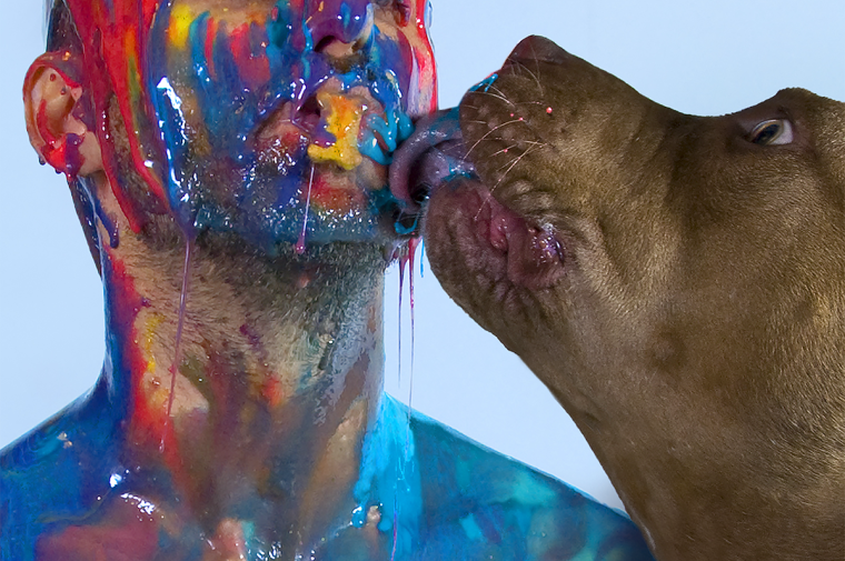 Self-portrait of the artist covered in brightly colored viscous liquid with a dog licking his face 