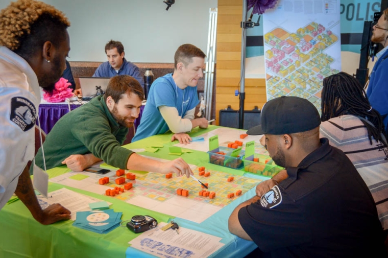 A multiracial group of people seated around a table with maps laid out
