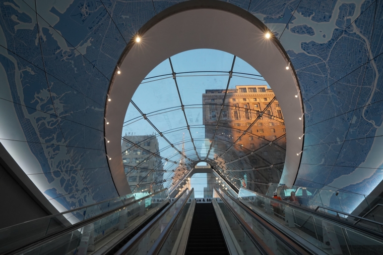 An escalator to the street features a glass oculus surrounded by a map of NYC in tiles