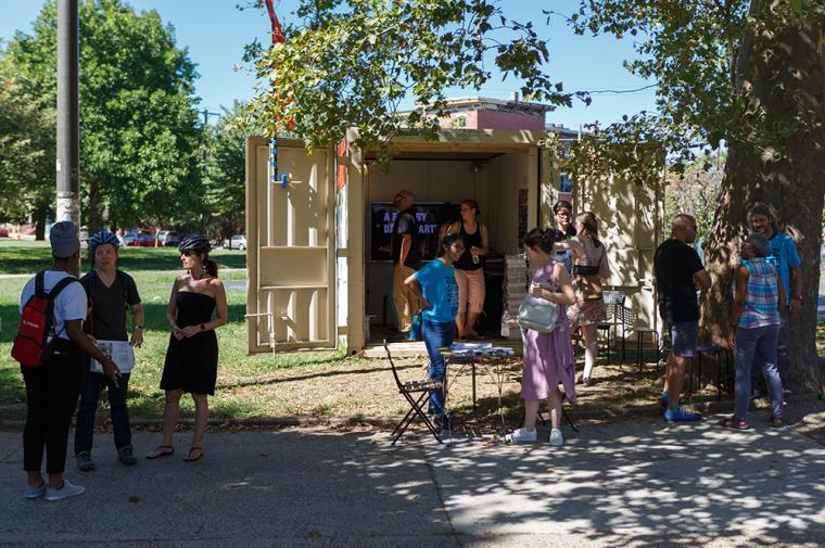 A group of young people standing outside a shipping container in a park