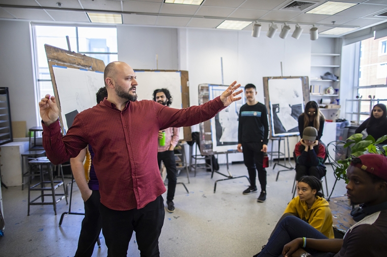 A man leads a discussion with students in an art studio