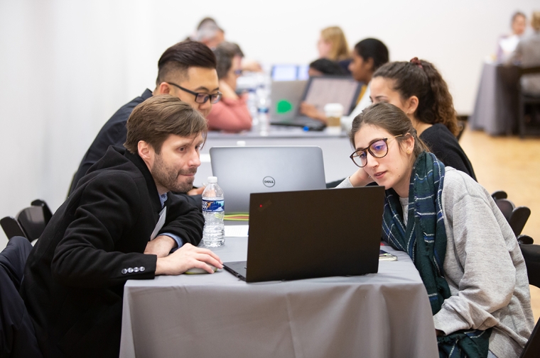 Alumni reviewers discuss student work on laptops with students.