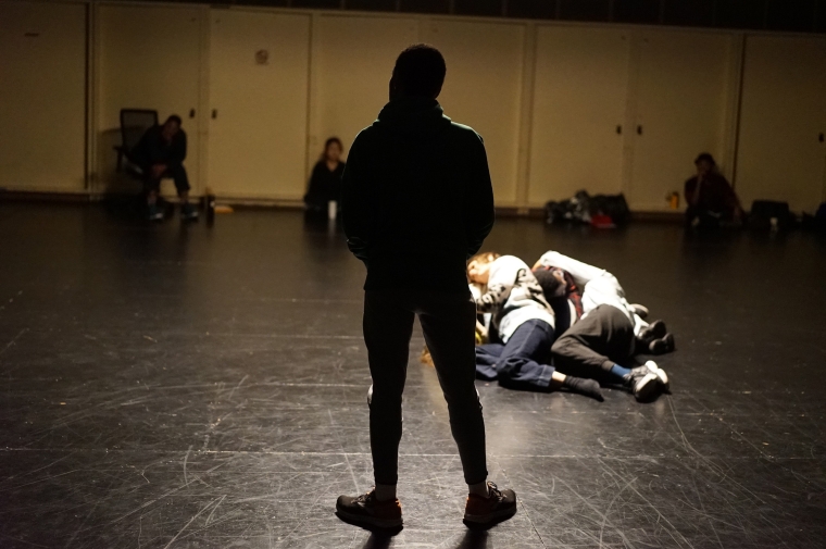 Two students lie on floor and one student with back to camera observes.