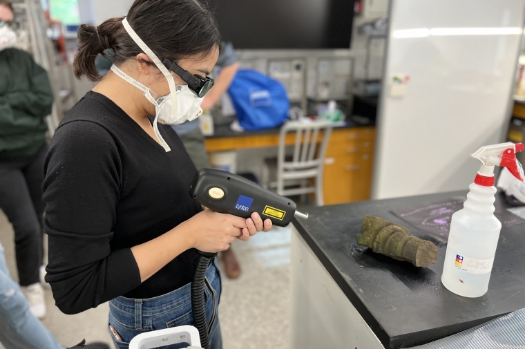 person points laser at stone carving wearing mask and goggles