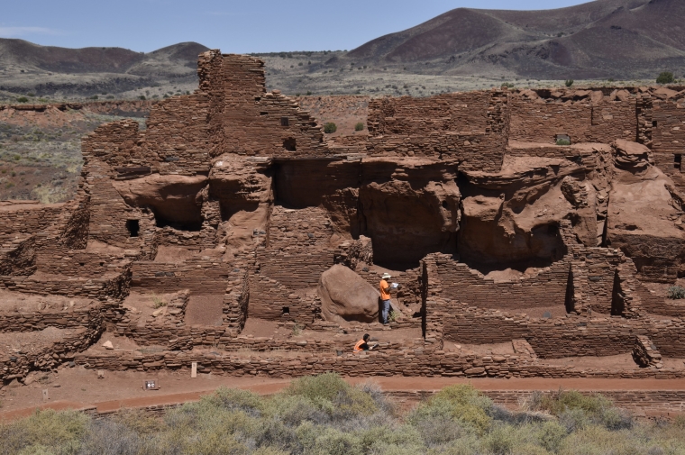 Two people make repairs to sprawling adobe brick construction in desert landscape