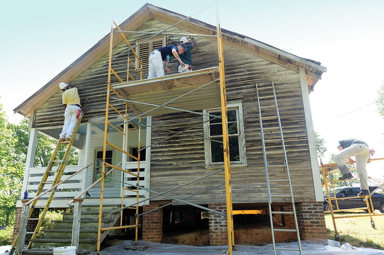 White wooden sided two story home with workers on scaffolding in front