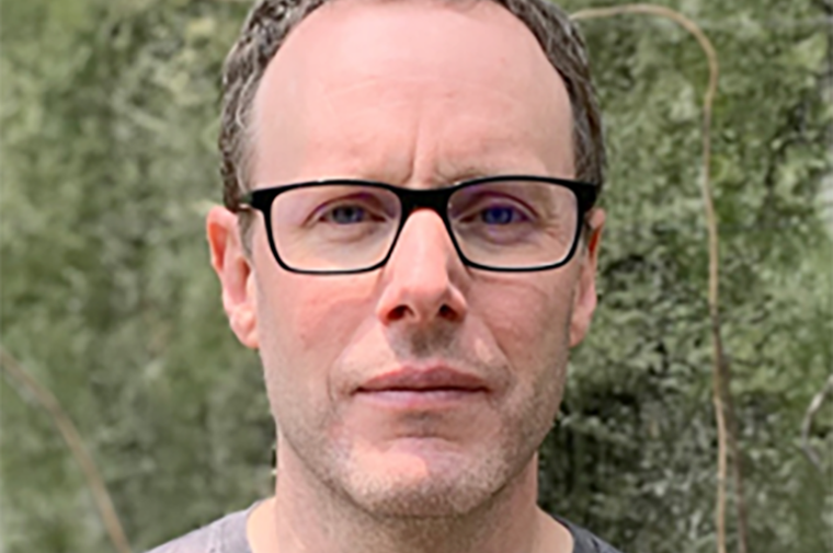 Photograph of Roger White in front of green, organic-looking wall 