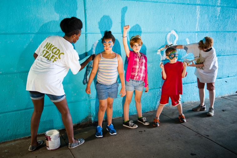 Team members Nyasha Felder and Emily Silber contribute to the interactive mural with community children