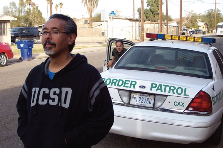 Dominguez looking off camera as a border police officer exits their car behind him