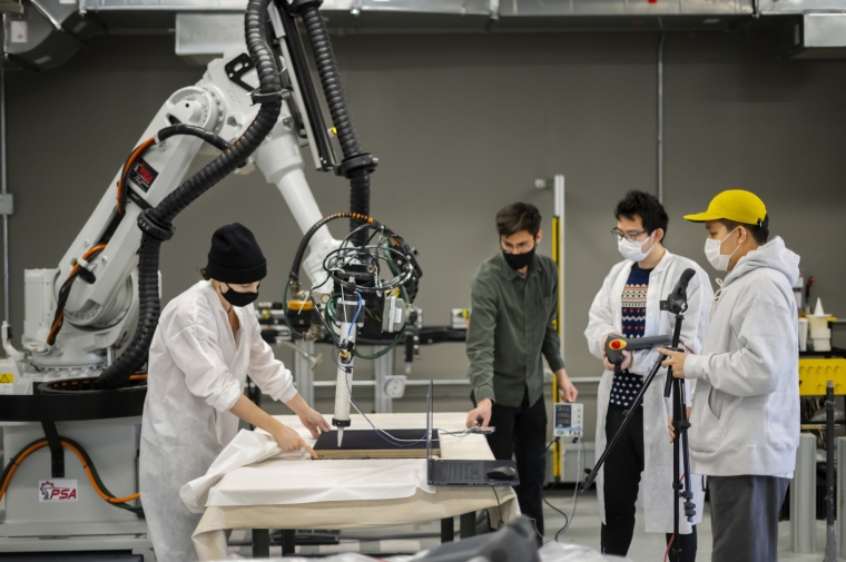 A group of people in lab coats work with a robotic arm