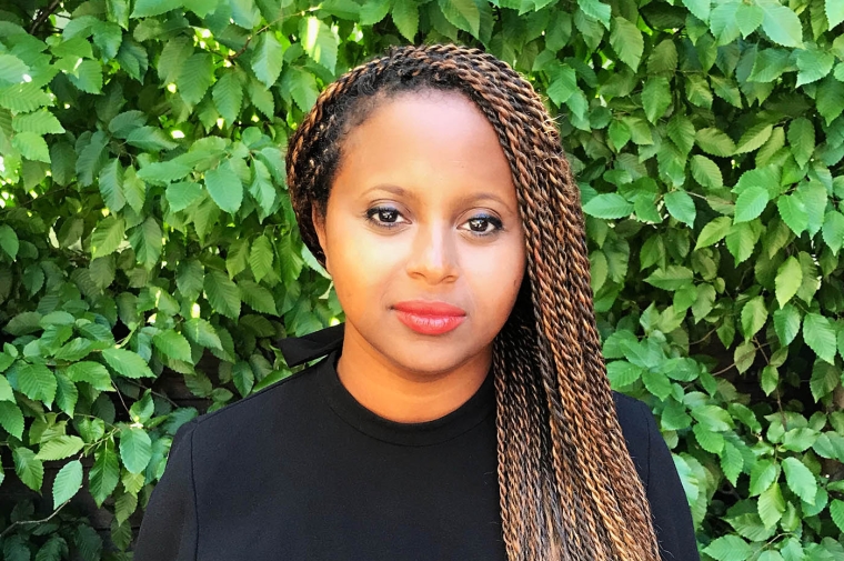 Sara Zede is pictured in a black sweater in front of a background of green shrub