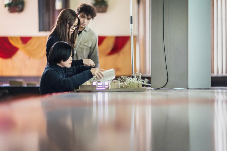 Three young people huddled over white architectural model