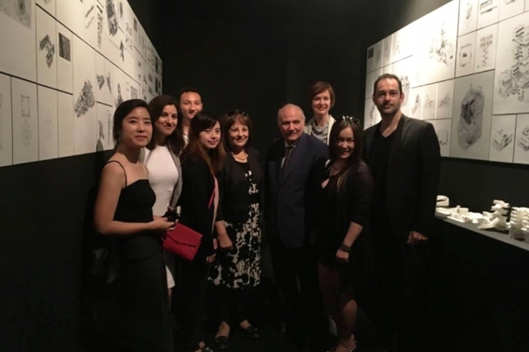 Faculty and students facing the camera in a darkened corridor lined by renderings