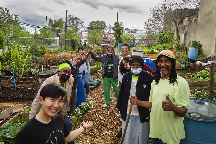 A group of people of various ages and ethnicities stand in a community garden